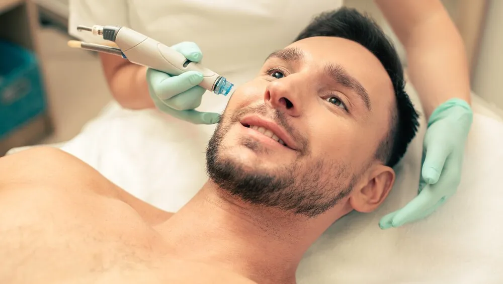 close-up-young-bearded-man-looking-glad-with-modern-tool-near-his-face-nourishing-skin